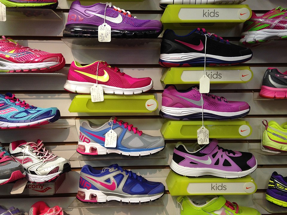  A variety of running shoes for kids and adults in bright colors are arranged on shelves in a store.